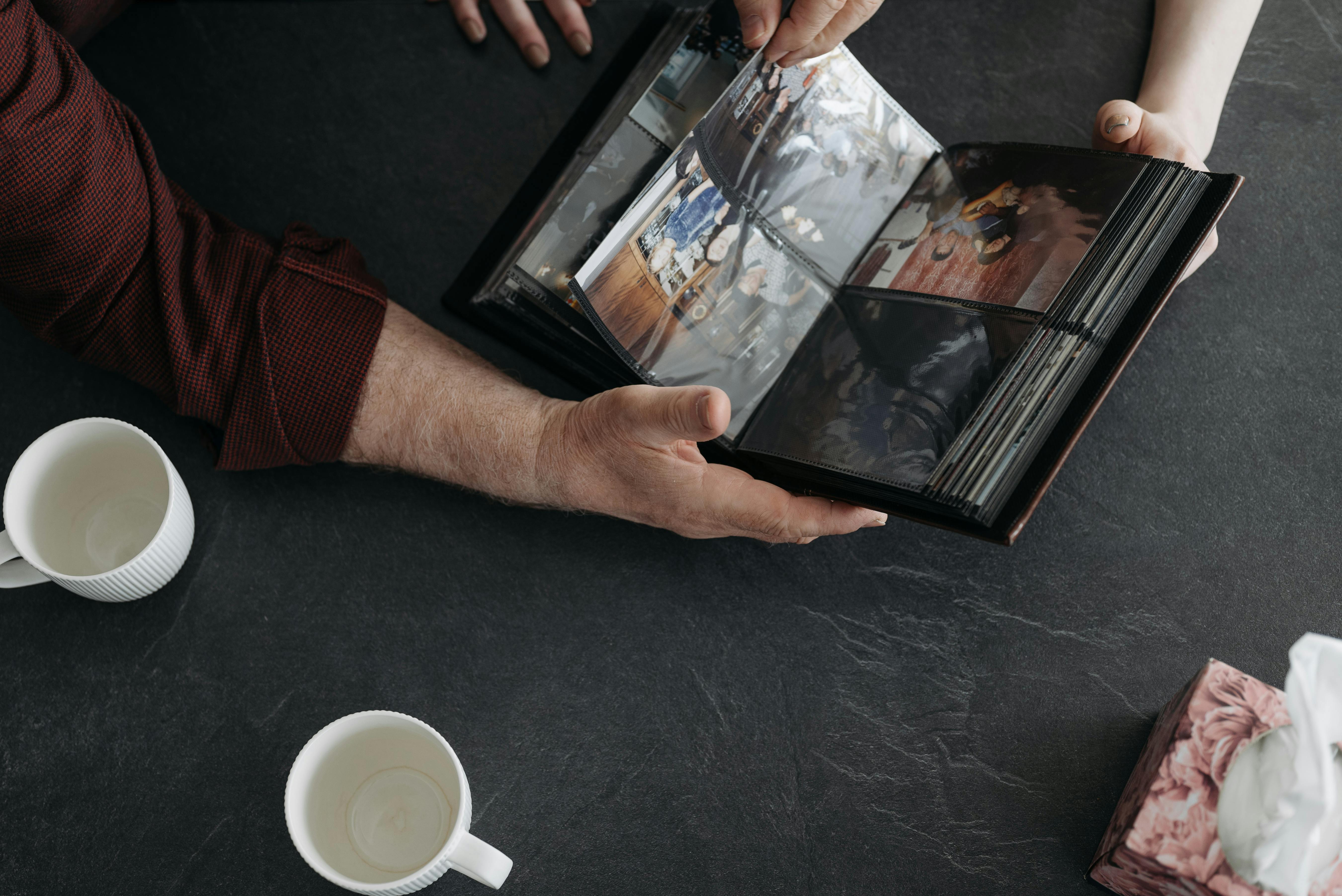 Hands holding a photo album with coffee cups, evoking memories and nostalgia.
